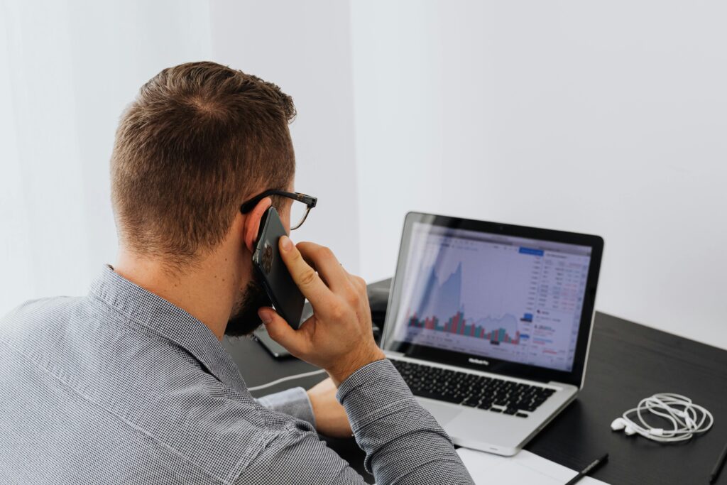 Businessman analyzing stock market data on a laptop while talking on the phone at his desk.