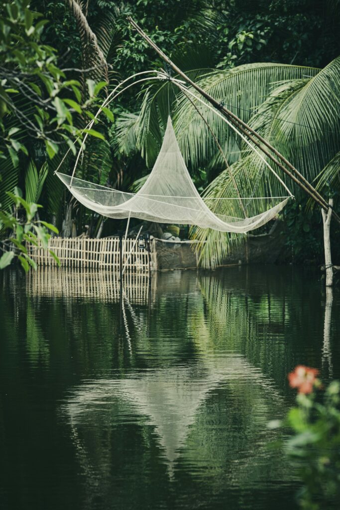 A traditional fishing net is suspended over a tranquil tropical pond surrounded by lush greenery.